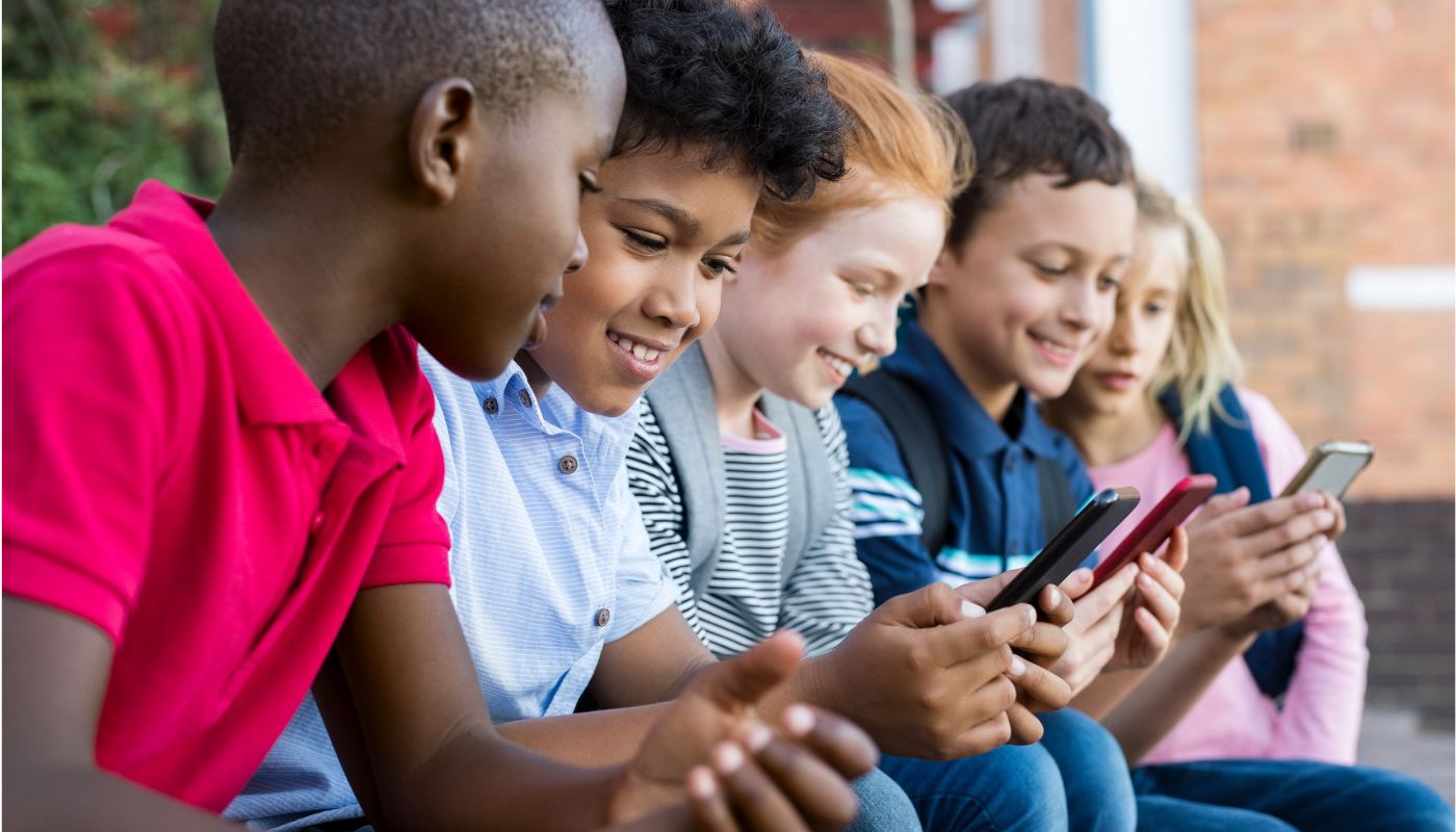 A group of children smiling and looking at their phones